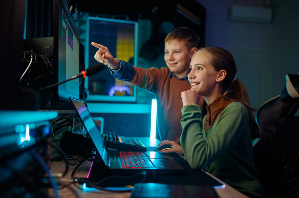 Children young musician working with soundtrack on computer sitting front of monitor at recording studio